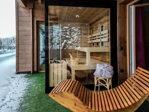 Una cabaña de madera con puerta de cristal, un banco de madera y una pequeña mesa con una toalla encima.