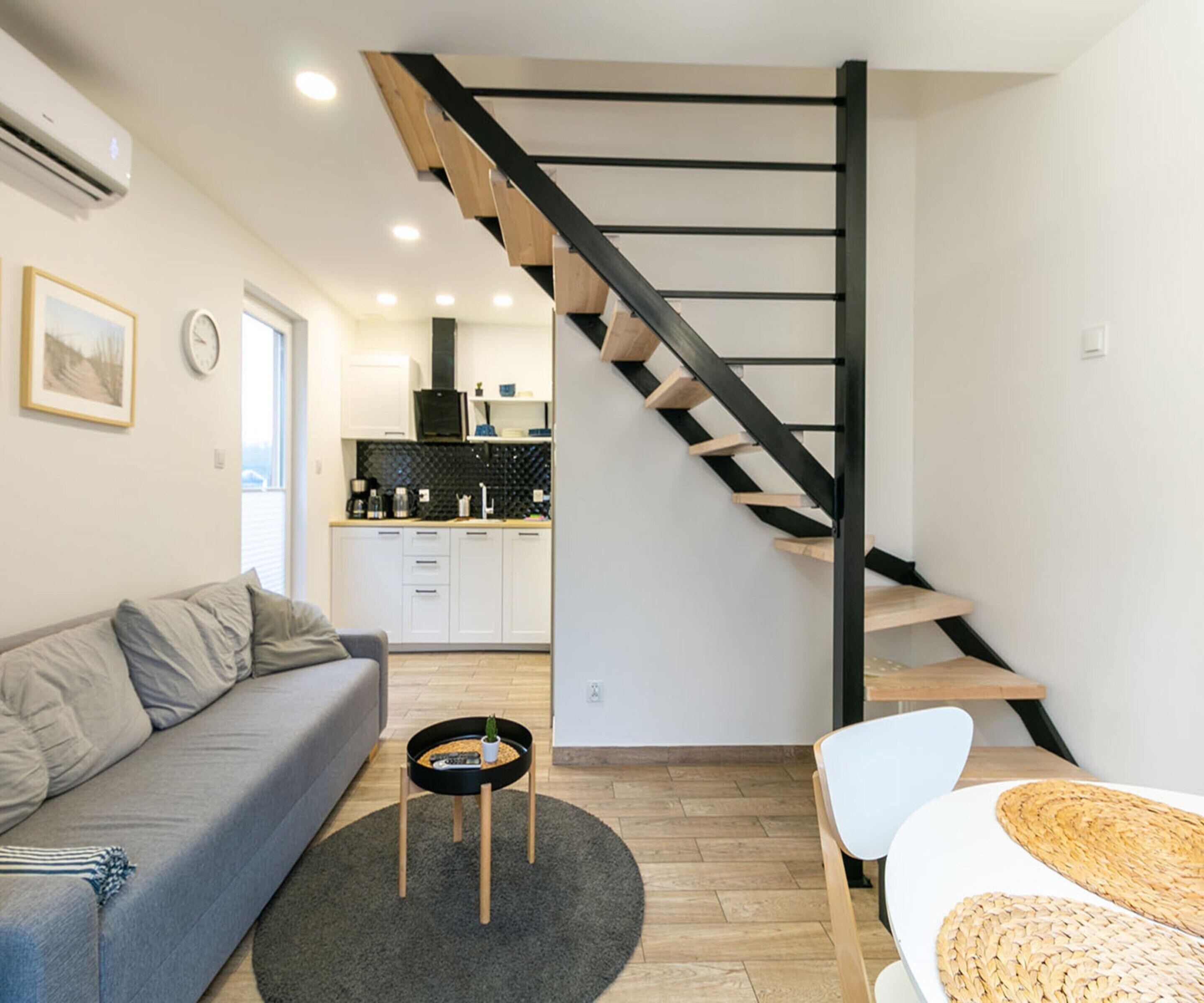 A modern living space with a staircase, a sofa, a coffee table, and a kitchen in the background.