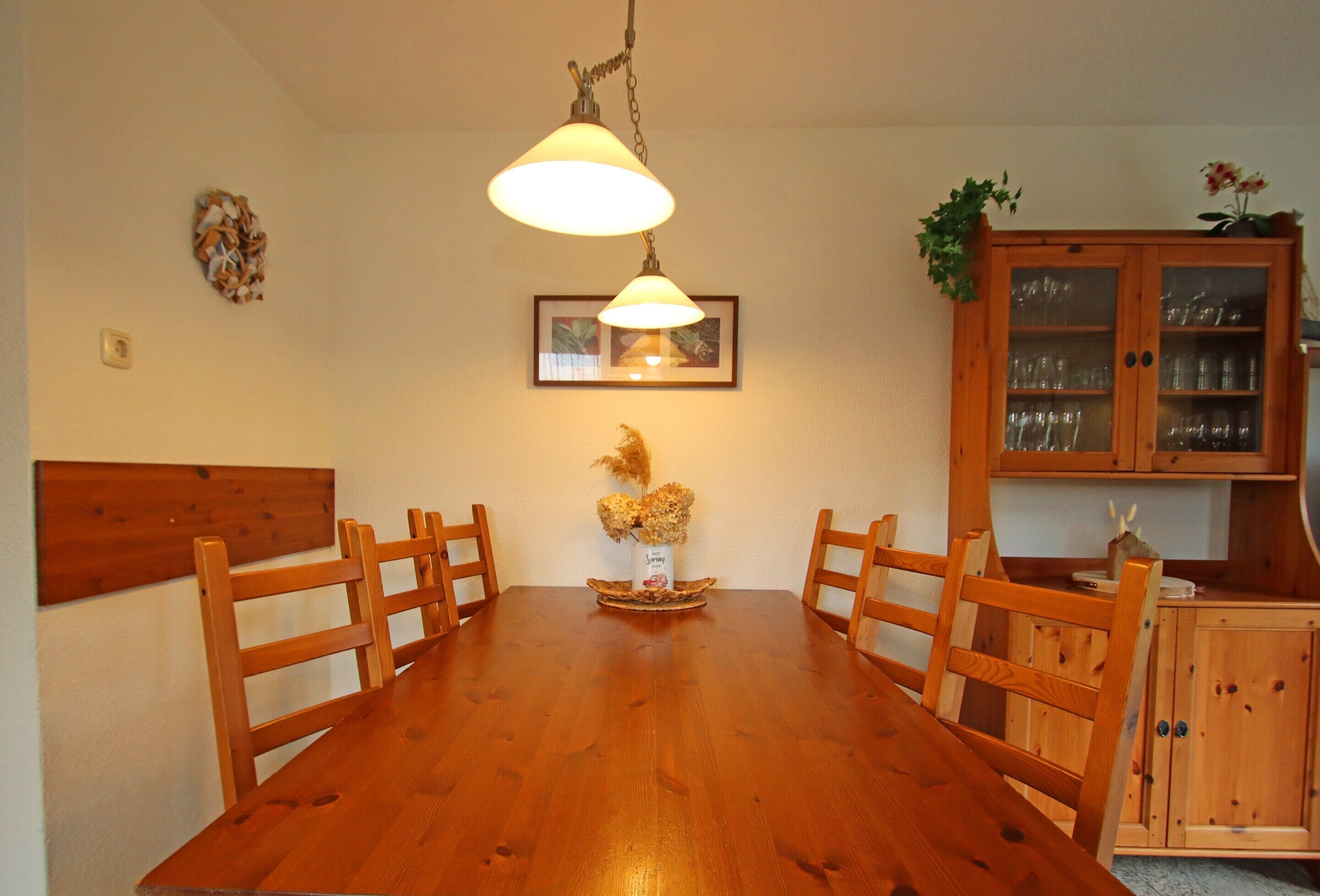Een eetruimte met een houten tafel, stoelen, een hanglamp, een kast met glazen deuren en een ingelijst kunstwerk aan de muur.