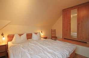 A bedroom with a bed, nightstands, a wooden wardrobe, and a chair. - Doppelhaushalfte, Zingst (Zingst)