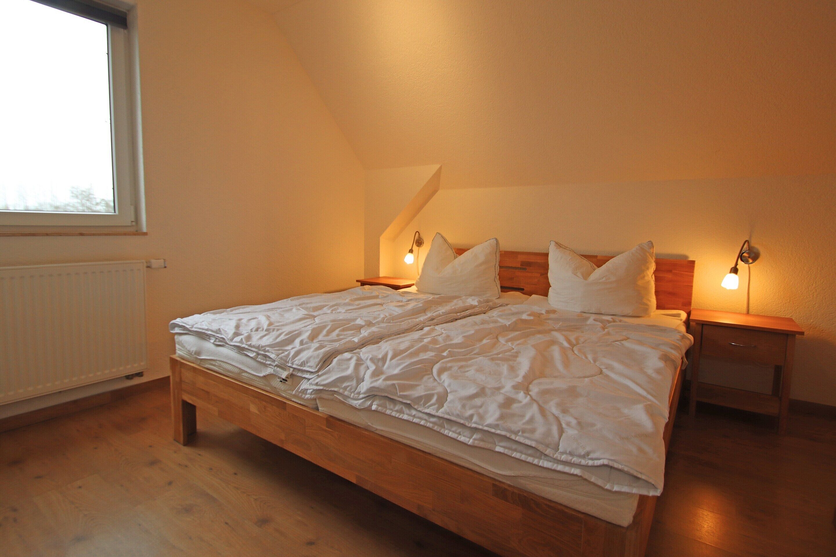 Un dormitorio con una cama de madera, dos mesitas de noche, una ventana y un radiador.