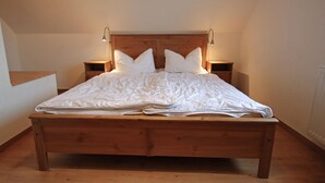 A large wooden bed with white bedding in a room with sloped ceilings and wooden headboard. - Doppelhaushalfte, Zingst (Zingst)