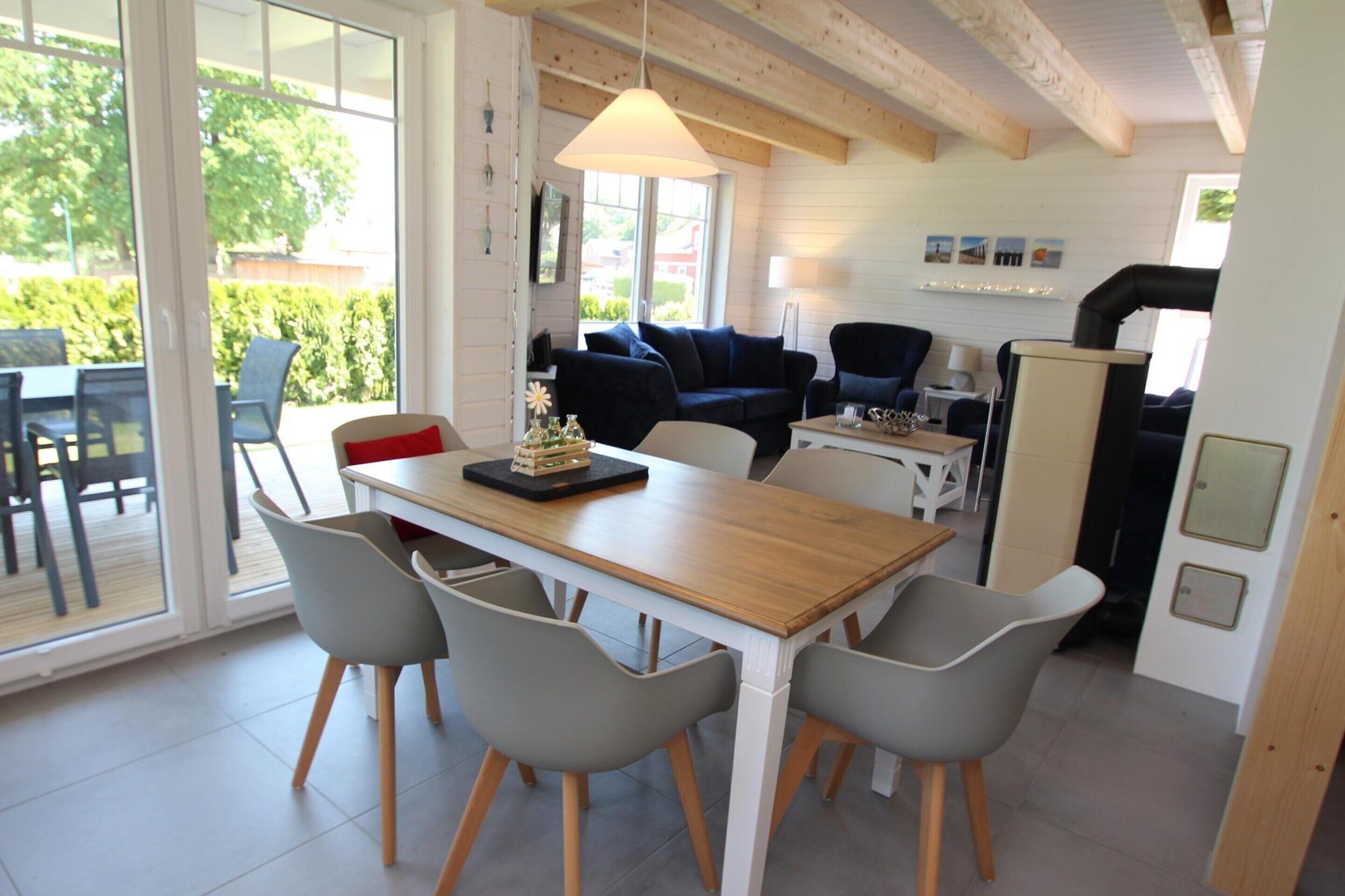 A modern kitchen with a wooden table and grey chairs, a sofa, and a dining area with a view of the outdoors.
