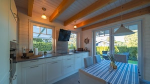 Eine moderne Küche mit weißen Schränken, ein Essbereich mit gestreifter Tischdecke und große Fenster mit Blick ins Freie.