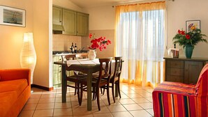 Ein Essbereich mit Tisch für vier Personen, eine Küche mit grünen Schränken und ein Wohnzimmer mit gestreifter Couch.
