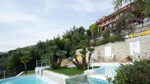 Ein Swimmingpool mit Steinmauer und Rasenfläche, umgeben von Bäumen und einem Gebäude mit Balkonen.