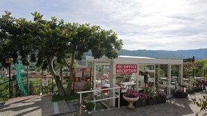 Ein Außenbereich mit Empfangsbereich, einem Schild mit der Aufschrift 'Office Reception', einem Glastür-Eingang und Blick auf die umliegende Landschaft.