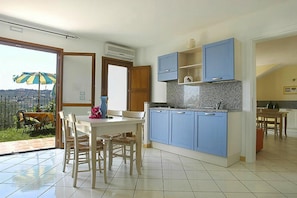 A modern kitchen with blue cabinets, a dining area with a table and chairs, and a view of a cityscape through a glass door. - Apartment in the Villa Giada Holiday Complex in Imperia (Imperia)