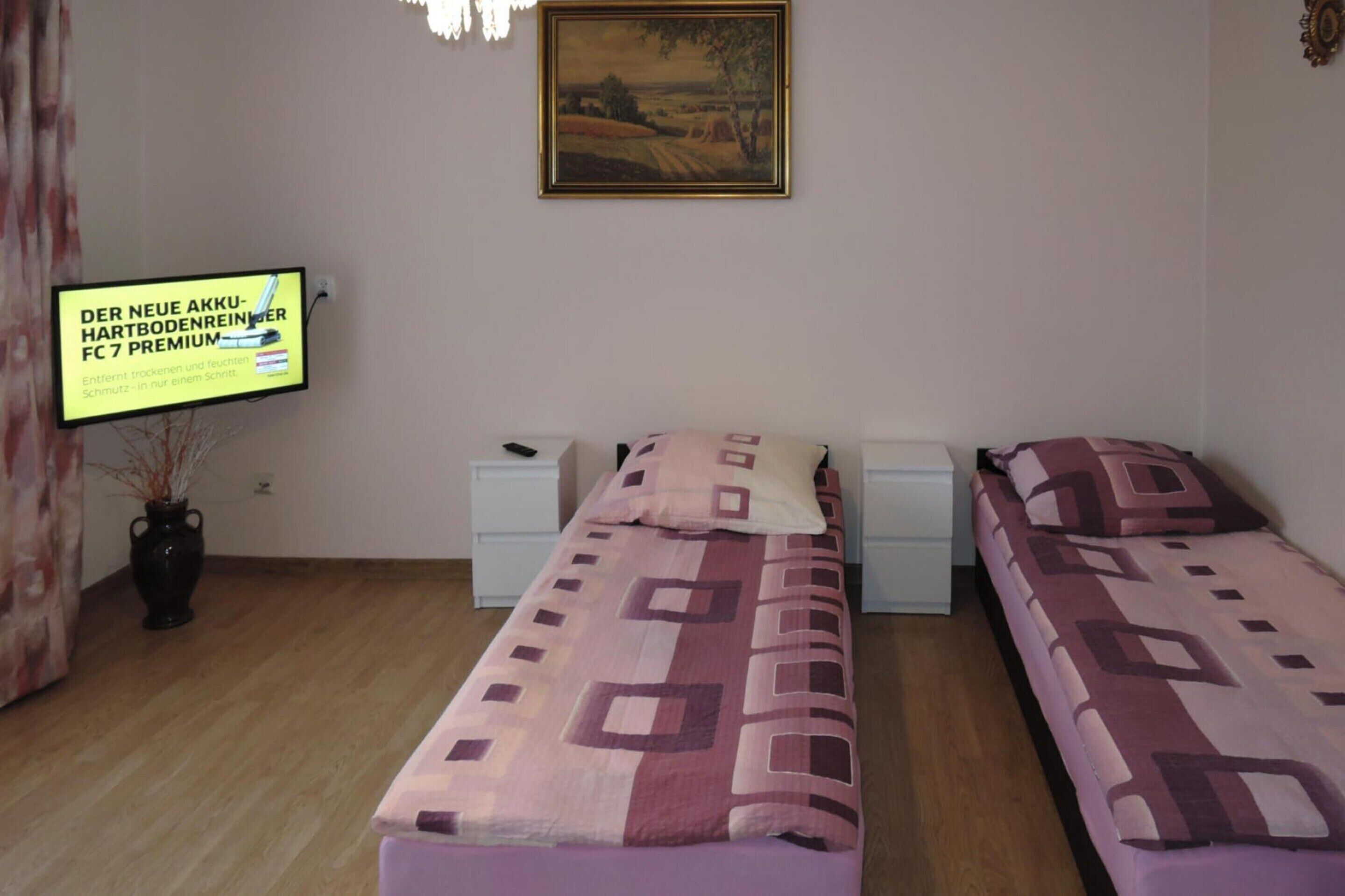 Ein Zimmer mit zwei Betten, einem an der Wand befestigten Fernseher und einer Vase mit Trockenpflanzen.