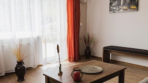 A living room with a wooden coffee table, a bench, a vase with dried plants, and a painting of a city street.