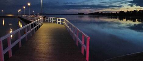 A wooden pier extending into calm water, illuminated by evenly spaced street lamps.