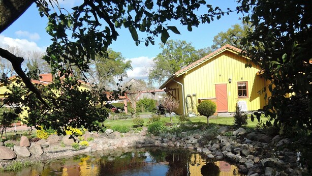 A yellow building with a pond in front, surrounded by rocks and plants. - House in Stepnica With Sauna and Jacuzzi (Stepnica)