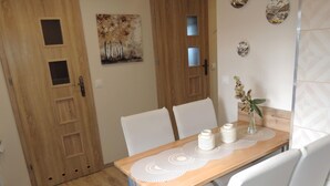 A dining area with a wooden table, white chairs, and a decorative runner. There are two wall-mounted light fixtures and a painting above the table. - House in Stepnica With Sauna and Jacuzzi (Stepnica)