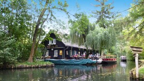 A riverside building with a dock, surrounded by trees and greenery. - Apartments Spreeidyll, Schlepzig (Schlepzig)