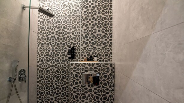 A shower area with a patterned wall, a glass door, and a metal towel rack. - Ocean 11 Hotel (Skiathos)