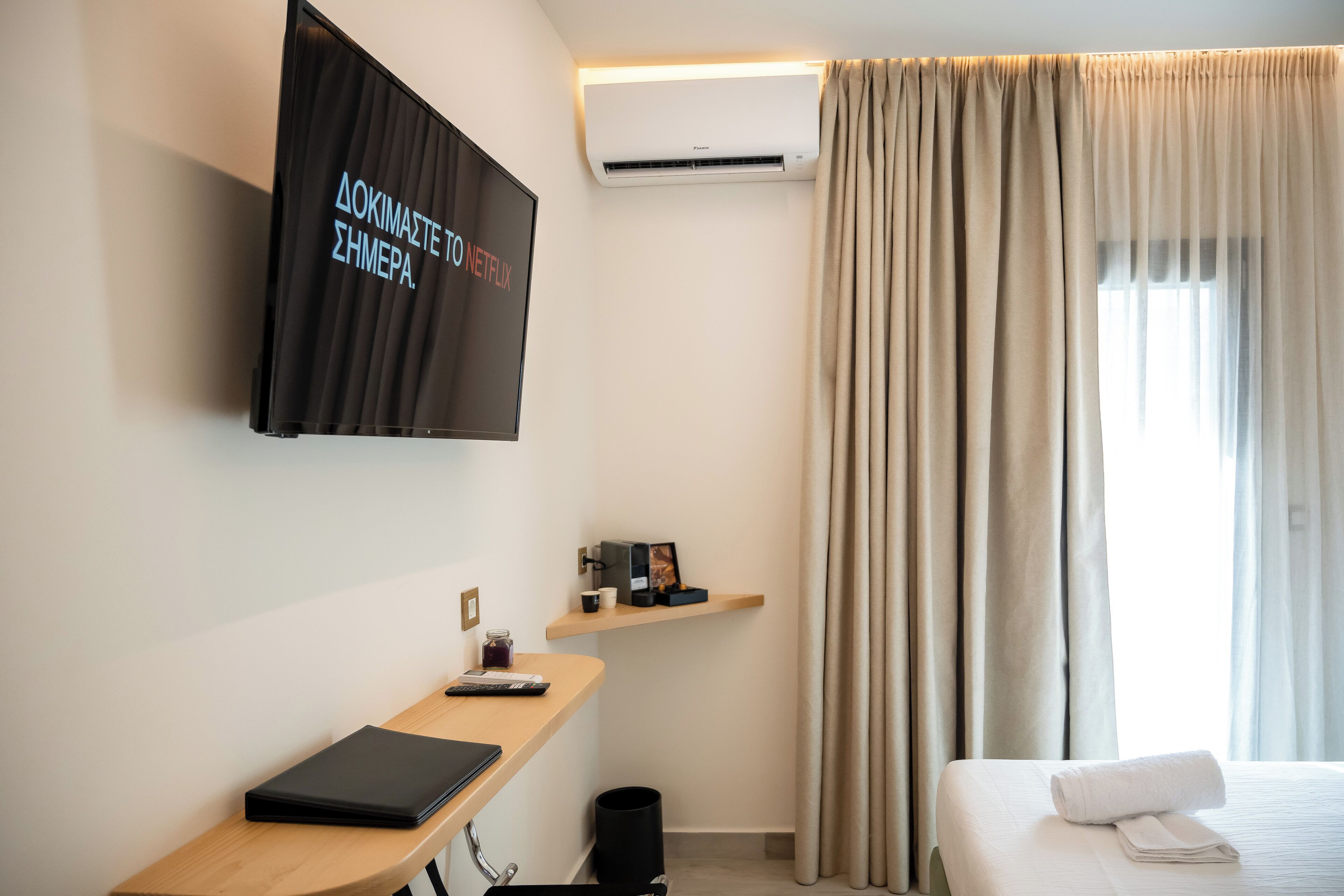 Une chambre d’hôtel moderne équipée d’une télévision à écran plat, de la climatisation, d’un bureau avec un ordinateur portable, d’un lit avec une serviette roulée et d’une fenêtre avec des rideaux.