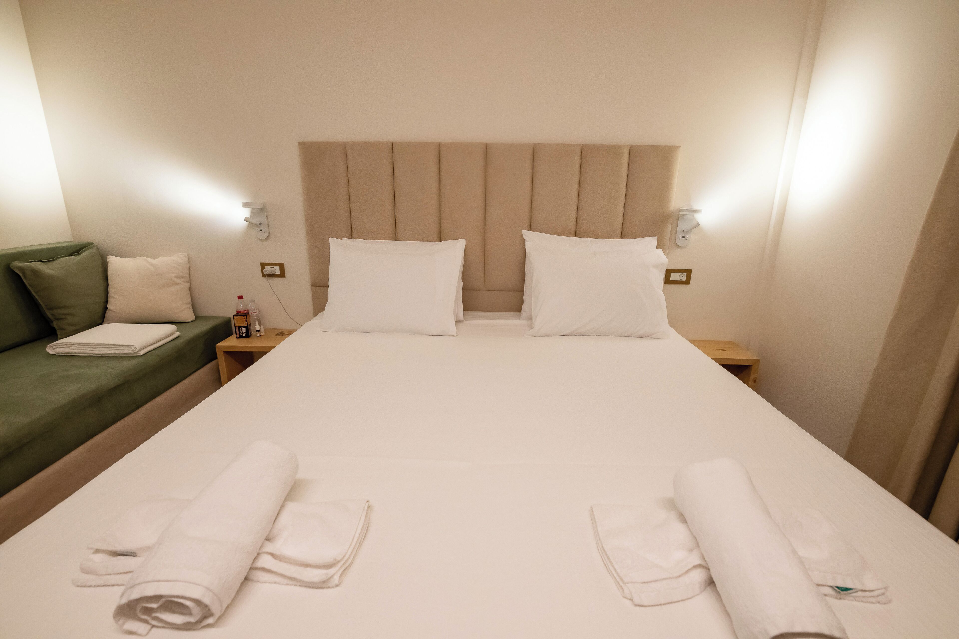 Une chambre d’hôtel avec un grand lit, deux tables de chevet, un canapé vert et un luminaire fixé au mur.