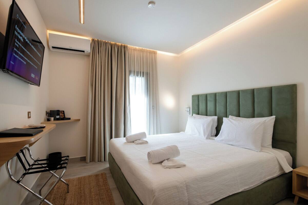 A modern hotel room with a large bed, a desk with a chair, and a flat-screen TV mounted on the wall.
