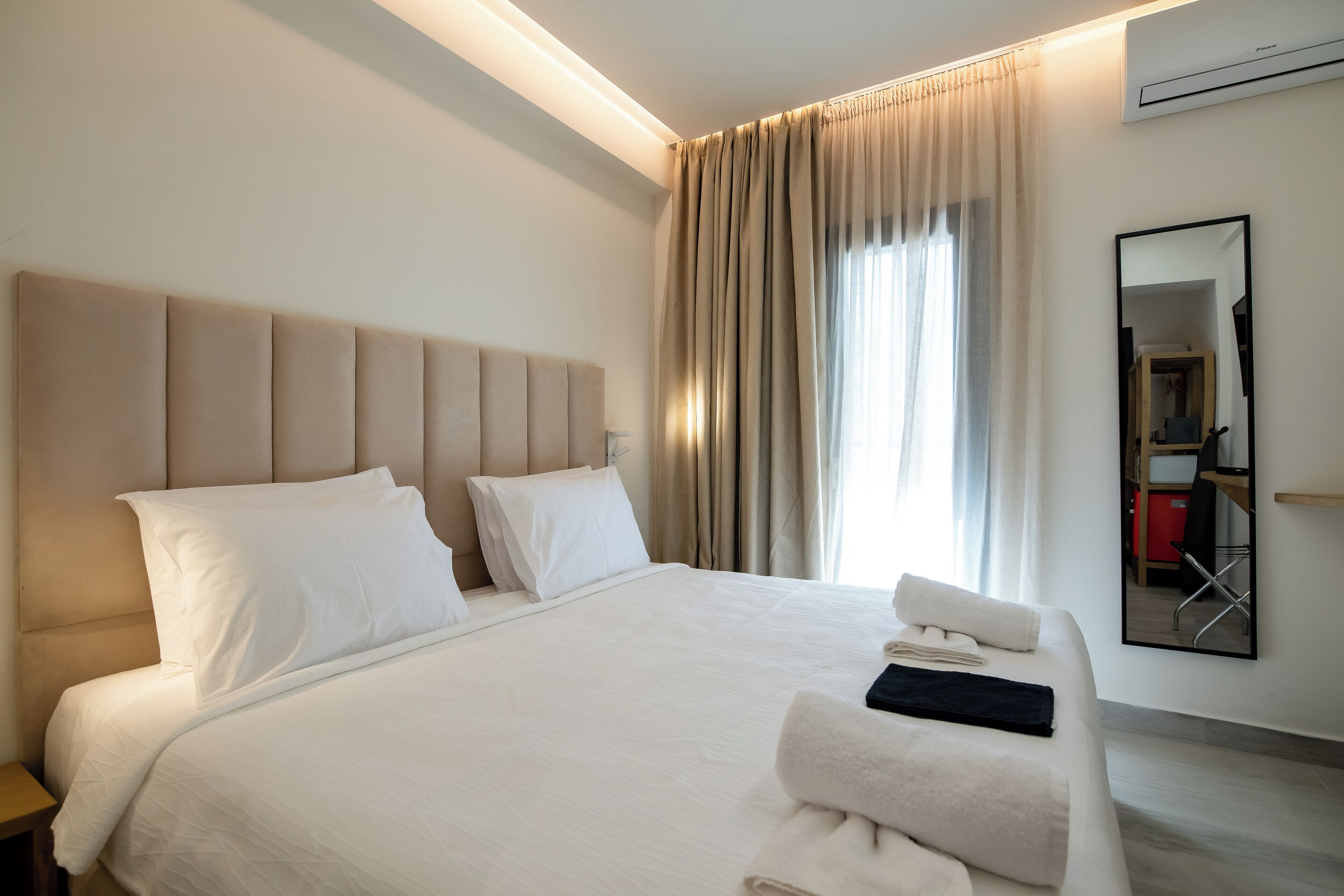 Habitación de hotel con una cama grande, una mesita de noche, un espejo y vistas al pasillo.