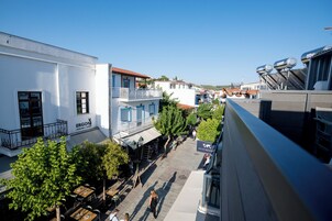 Vista de la calle con mesas al aire libre, un edificio blanco con balcón y un cartel que dice 'ERGON'.