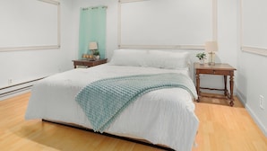 A bedroom with a large bed, two bedside tables, a nightstand, a teal curtain, and a wooden floor. - Spacious 4 bdrm home, Close to Lake, Wine, Downtown, Kid Friendly, Self Checkin (Geneva)