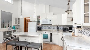 A modern kitchen with white cabinetry, a built-in microwave, a coffee maker, and a dishwasher. There are two bar stools and a small island with a sink. - Spacious 4 bdrm home, Close to Lake, Wine, Downtown, Kid Friendly, Self Checkin (Geneva)