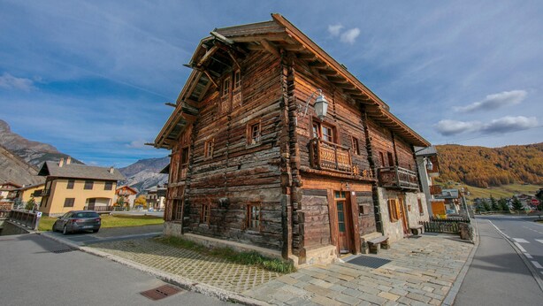 Un bâtiment traditionnel en bois, doté d’un toit en pente et d ’un balcon, situé dans une rue où une voiture est garée devant.