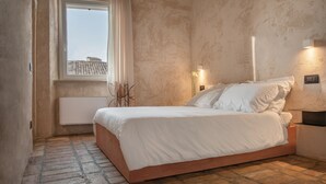 Een slaapkamer met een enkel bed, een raam met gordijnen, een radiator en een wandlamp.