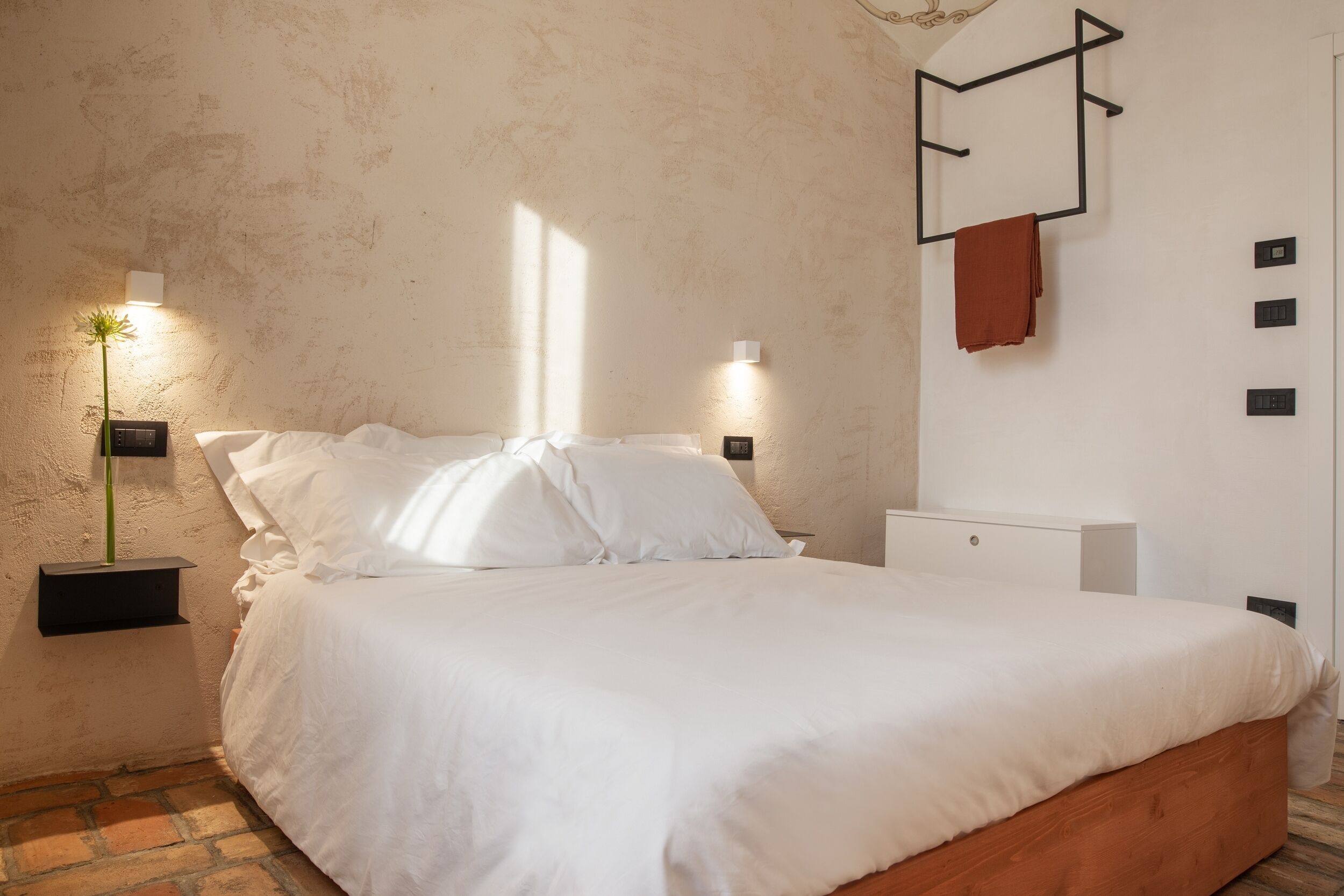 Une chambre à coucher comprenant un lit, des lampes de chevet, une table de chevet et un porte-serviettes fixé au mur.