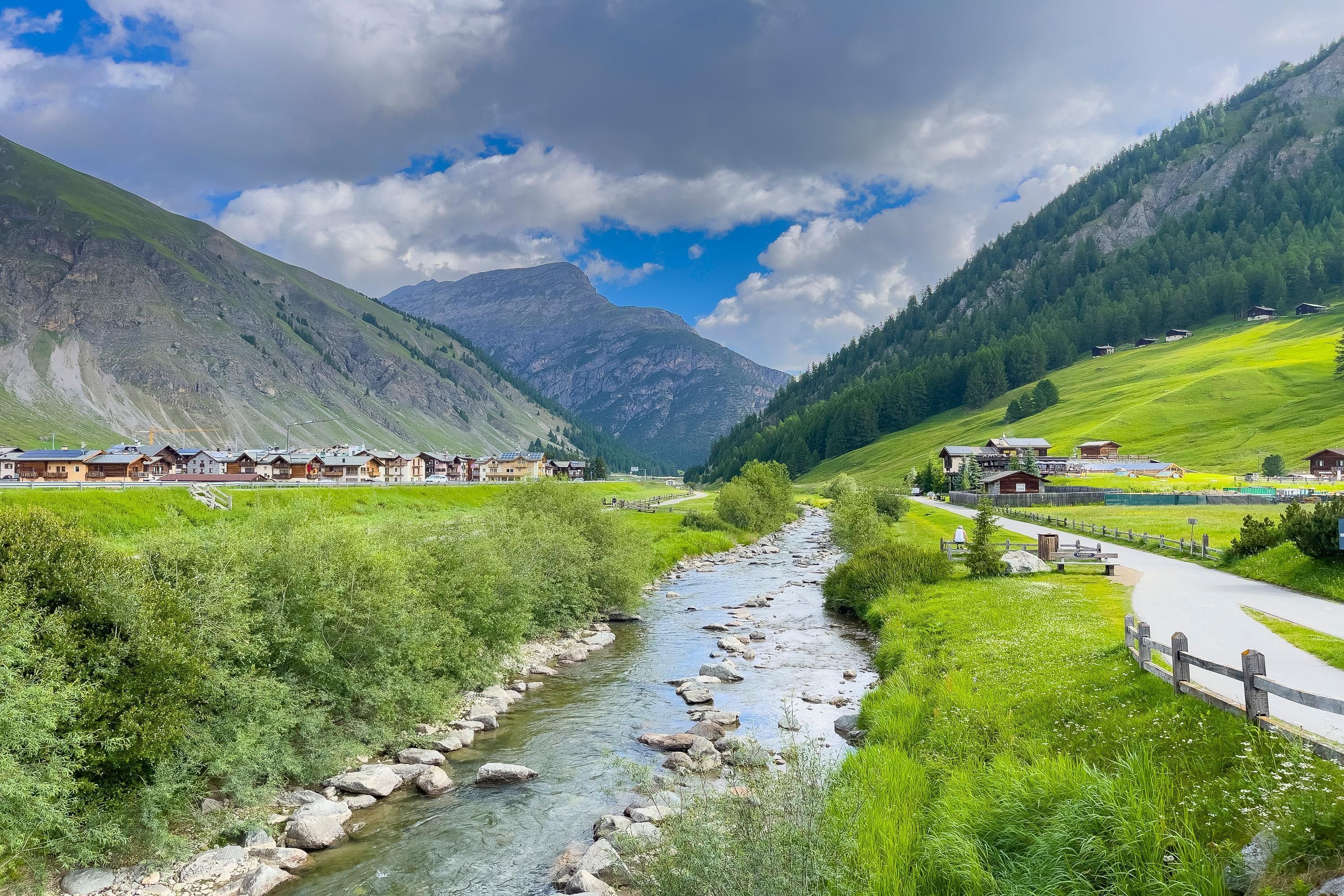 Un paisaje montañoso con un río, campos verdes y casas de madera.