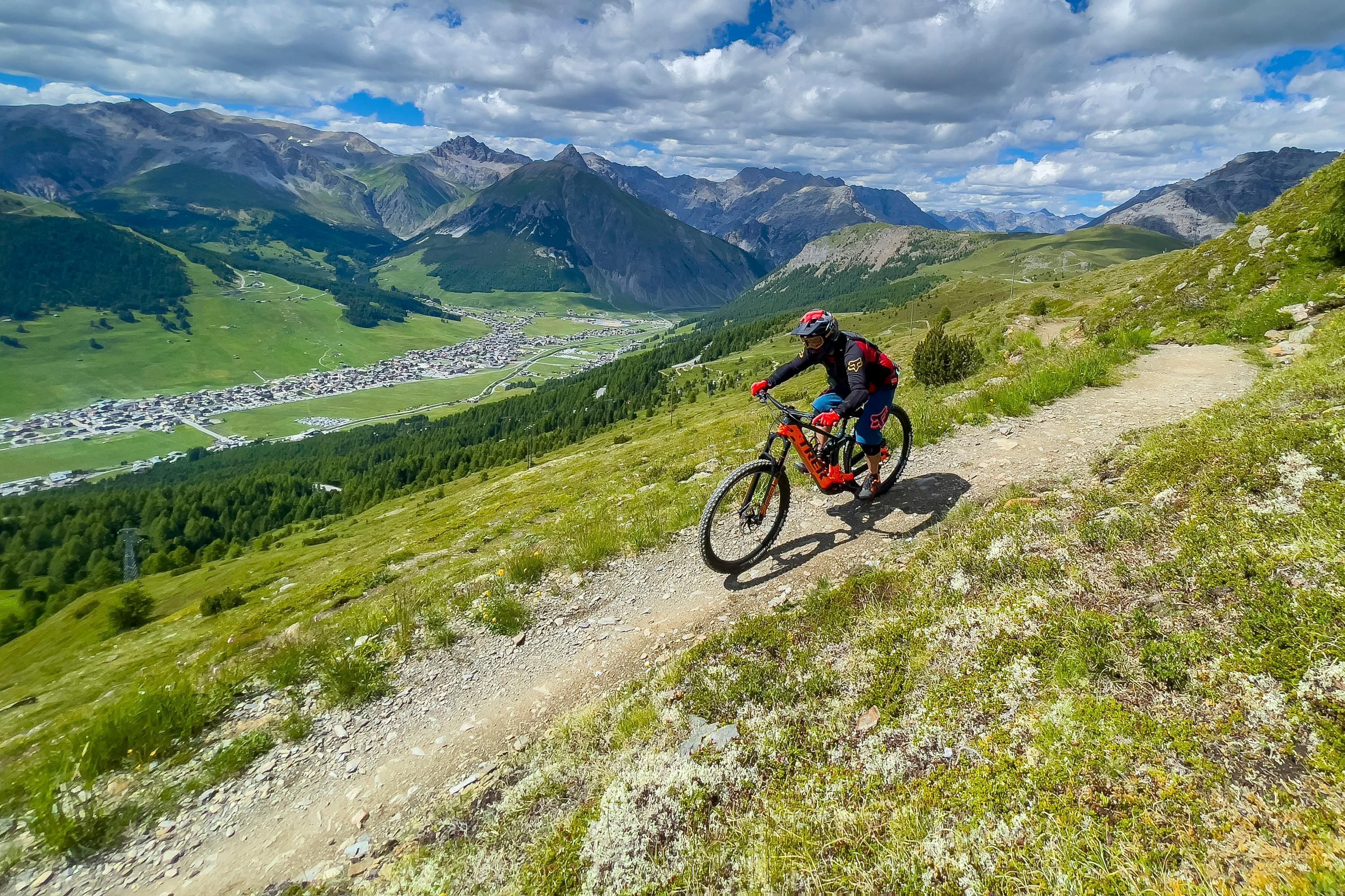 Un ciclista de montaña en un sendero de tierra con vistas a un valle y montañas al fondo.