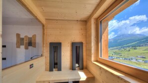 Een houten hut met een groot raam, een ingebouwde bank en uitzicht op een vallei.