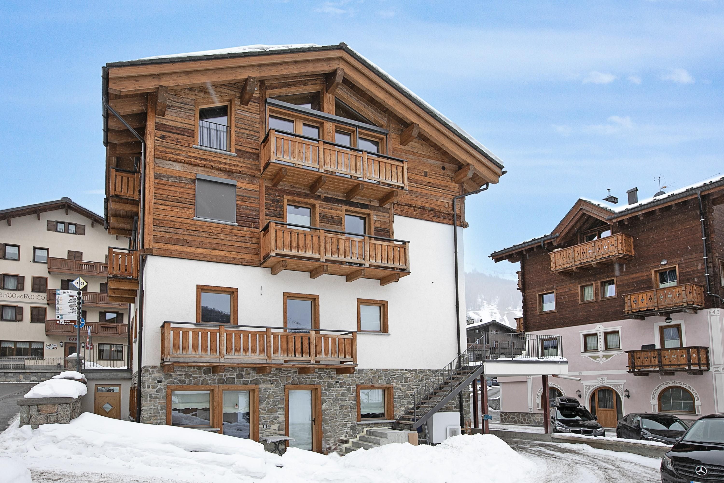 A multi-story wooden building with balconies, stone lower levels, and a snow-covered ground.