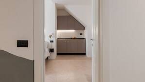 A narrow hallway leading to a kitchen with a sloped ceiling and a countertop with a kettle.