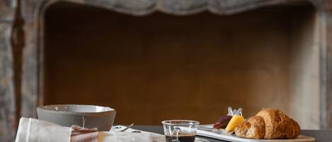 A breakfast setting with a bowl, a cup of coffee, a croissant, and fruit on a table.