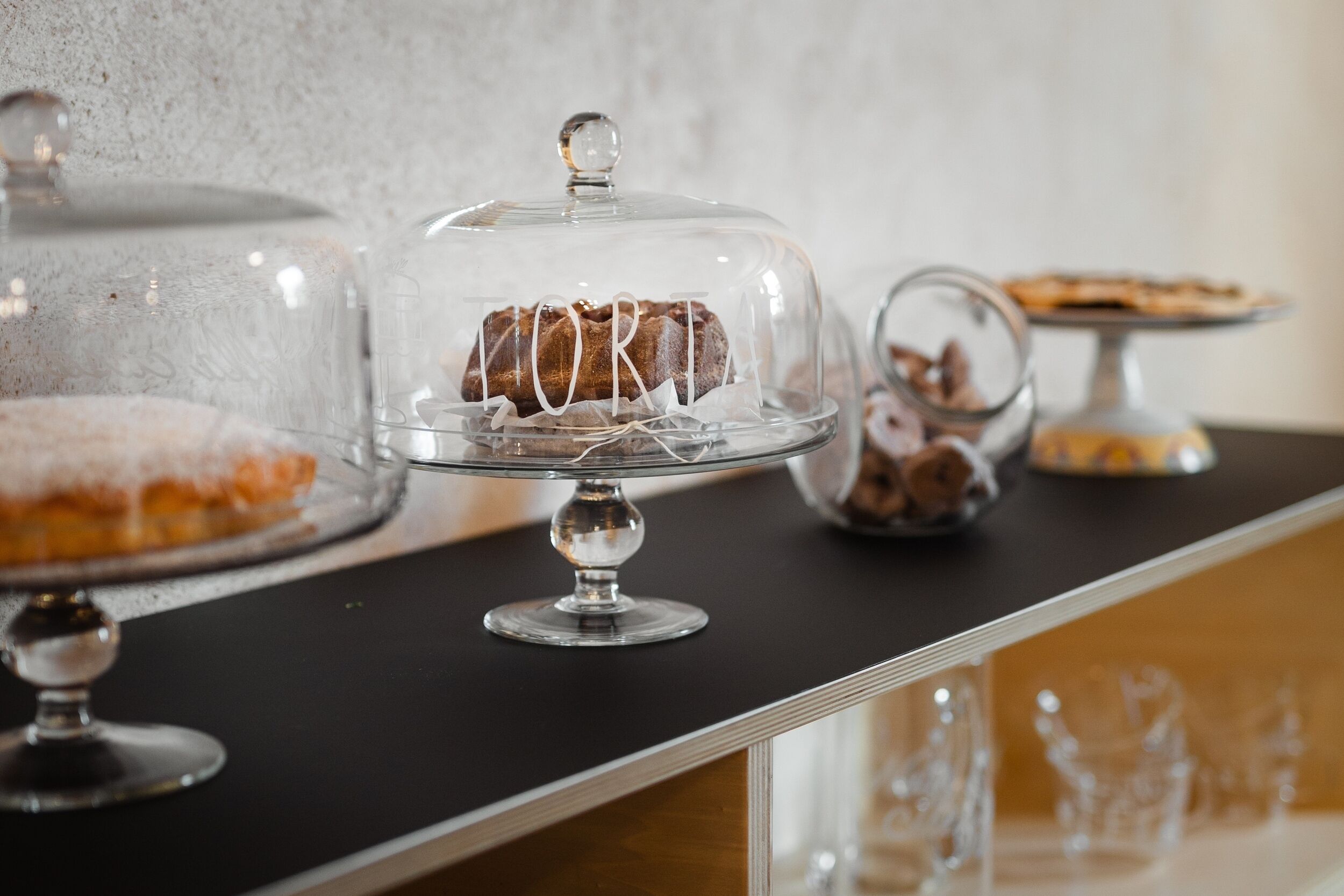 Mostra de postres amb diferents pastissos i forns dins de cloches de vidre sobre un taulell.