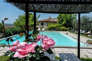 A pool area with a pergola, lounge chairs, and a house in the background. - Deliziosa Camera in Agriturismo a 7 km da Firenze (Toscana)