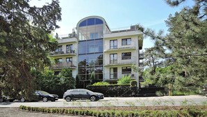 A multi-story building with a large glass facade, balconies, and a parking area with cars. - Holiday Appartment at the Promenade, Swinoujscie (Swinoujscie)