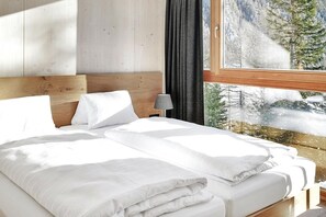 A bed with white linens, a wooden headboard, and a view of a snowy landscape through a window. - Chalet Resort in Kals am Grossglockner (Kals am Grossglockner)