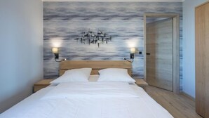 A bedroom with a bed, two bedside lamps, a wooden headboard, and a wall mural. - Penthouse am Nordstrand auf dem Deich (Nordstrand)