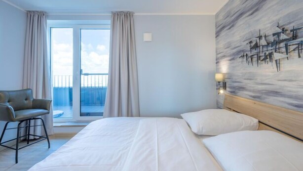 A hotel room with a large bed, a chair, a balcony with curtains, and a painting on the wall. - Penthouse am Nordstrand auf dem Deich (Nordstrand)