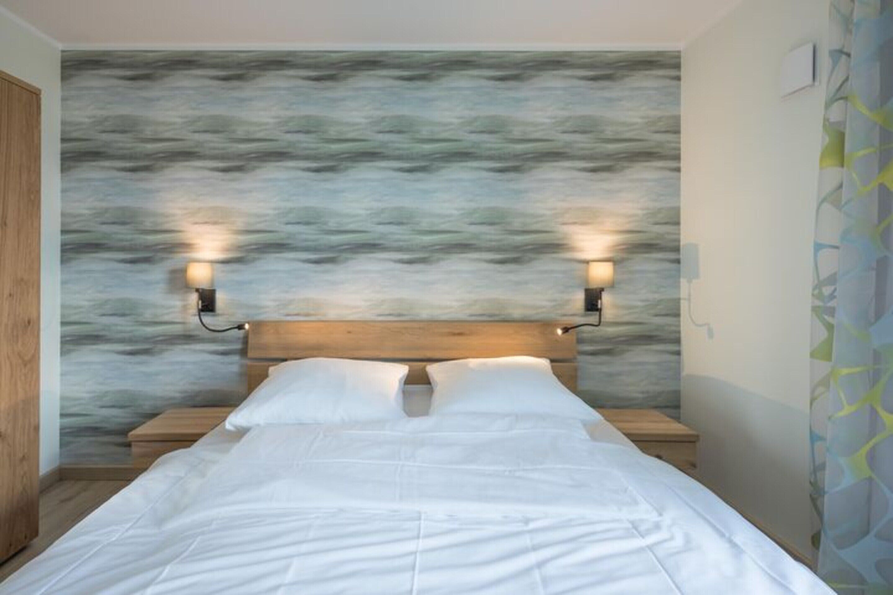 Un letto con una testiera in legno, due lampade sui comodini e una parete con un motivo astratto e materico.