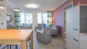 A modern living room with a wooden dining table, grey sofas, and a white cabinet. - Penthouse am Nordstrand auf dem Deich (Nordstrand)