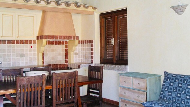 A dining area with a wooden table and chairs, a tiled backsplash, and a window with wooden shutters. - Apartment in Porto Rotondo Near the Beach (Olbia)