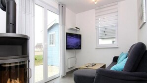 A modern living room with a fireplace, a sofa, a television, and a view of the outside. - Ferienhaus de Poeler Drift, Zierow (Zierow)