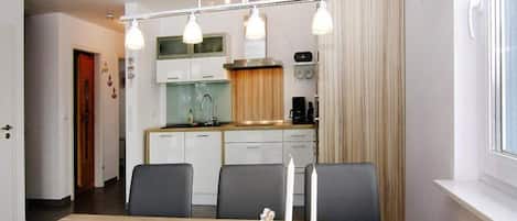 Una cocina moderna con armarios blancos, encimera de madera y horno empotrado. Hay una mesa de comedor con sillas y una carpeta azul encima.