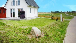 A two-story house with a white exterior and dark roof, a red garage, and a large rock in the foreground. - Ferienhaus de Poeler Drift, Zierow (Zierow)