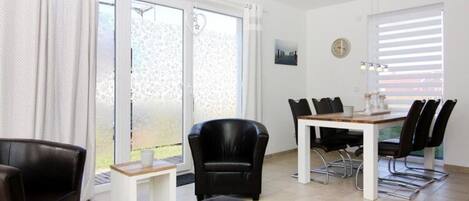 Un salon moderne avec un coin repas, comprenant un canapé, une table basse, une table à manger avec des chaises et une vue dégagée grâce à de grandes fenêtres.