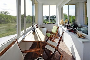 Ein sonnendurchfluteter Raum mit einem großen Fenster und Blick auf eine grüne Landschaft, einem Holztisch und mehreren Stühlen.