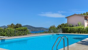 Ein Swimmingpool mit einer Metallleiter, umgeben von einer gefliesten Terrasse und einem Metallzaun.